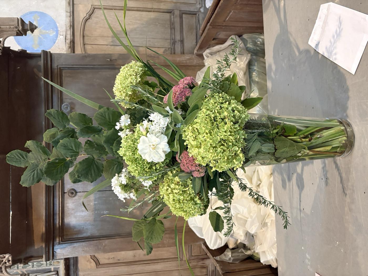Bouquet d’hortensias verts, de dahlias blancs et de feuillages, posé sur une table devant les boiseries du chœur.