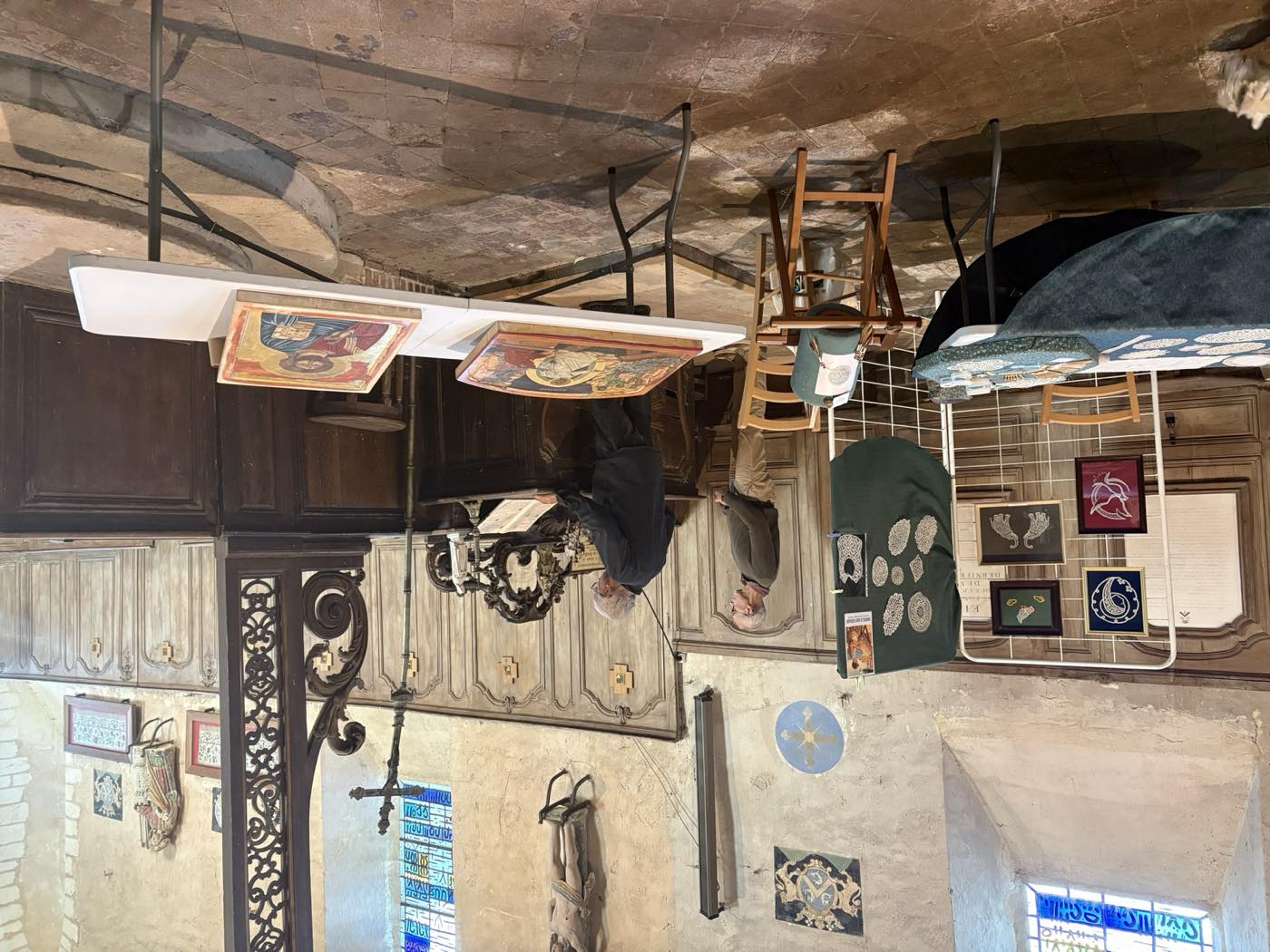 Dentelles encadrées, icônes peintes posées sur des tables et broderies accrochées sur une grille, devant les boiseries du chœur.